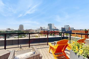 A balcony with orange chairs and a table overlooking a city skyline.